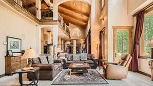 A spacious living room with a high ceiling, leather furniture, and a large window with curtains. - Stunning custom Home w/ private hot tub, quick drive to the slopes! (Keystone)