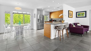 A modern kitchen with a central island, stainless steel appliances, and a dining area with clear chairs. - Stylish PS Home w/heated pool/spa & mountain views (Palm Springs)