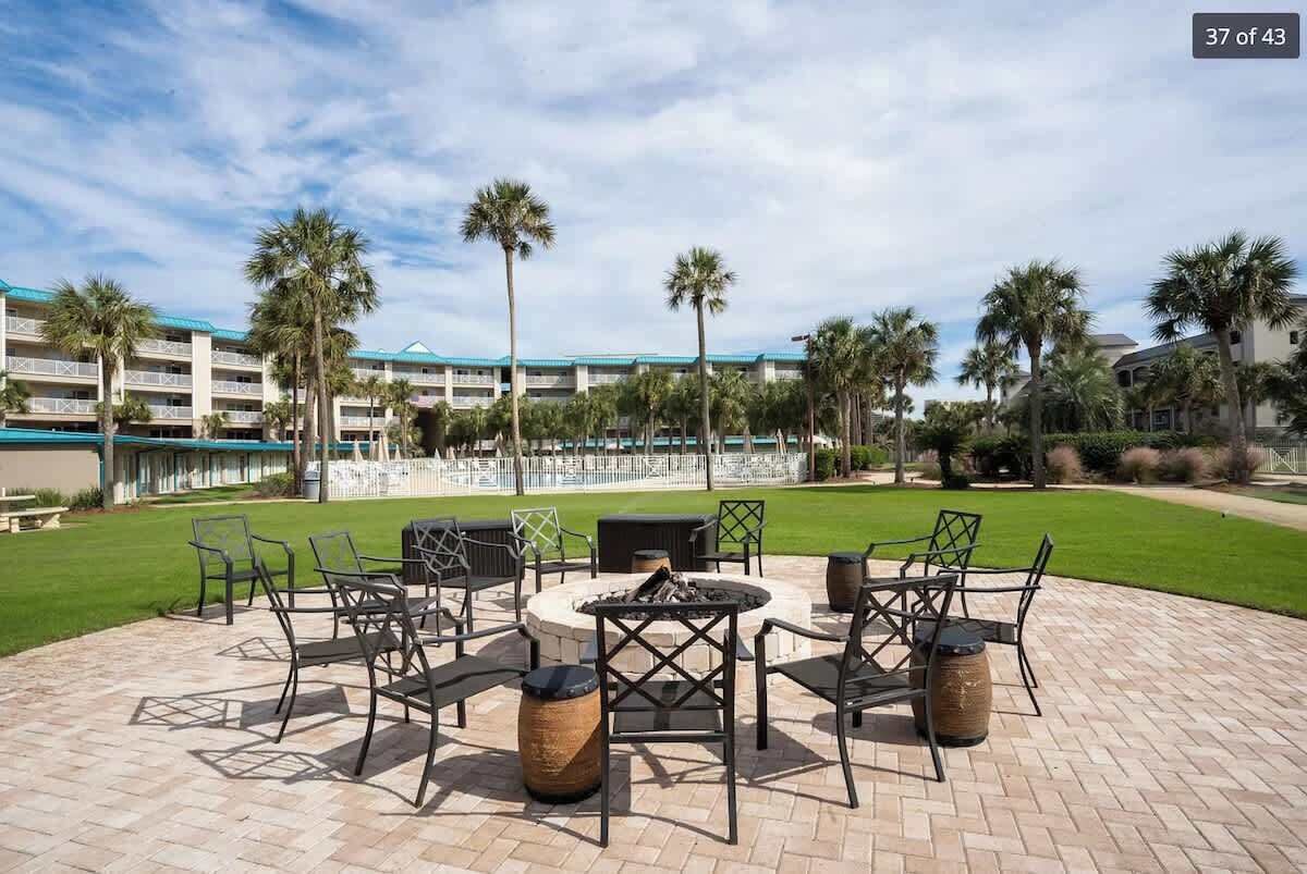 Eine Terrasse mit Sitzgelegenheiten im Freien, einem Feuerkorb und Blick auf ein Hotelgebäude mit mehreren Stockwerken und einem blauen Dach.