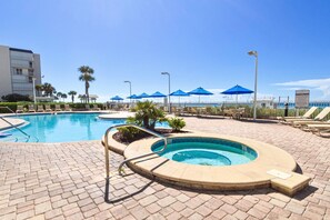 A pool area with a hot tub, lounge chairs, and umbrellas.