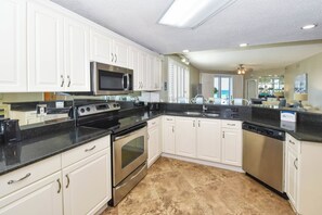 A modern kitchen with white cabinets, stainless steel appliances, and a black countertop. - Gulf-front First Floor Condo with Two Master Suites! (Destin)