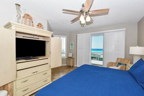 A bedroom with a bed, a ceiling fan, a TV, a dresser, a window with a view, and a chair.
