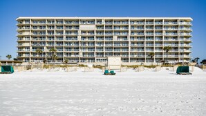 Een hotel met meerdere verdiepingen en balkons, gelegen aan een zandstrand met palmbomen.