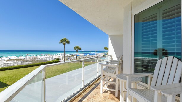 Een balkon met uitzicht op een strand, palmbomen en een helderblauwe lucht.