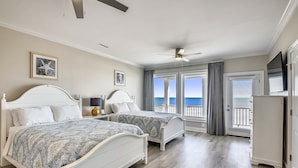 A bedroom with two beds, a ceiling fan, and a view of the ocean.