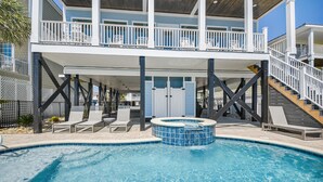 A swimming pool with lounge chairs and a hot tub, surrounded by a covered deck and stairs leading to an upper level with balconies.