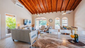 A spacious living area with a high ceiling, a television, a dining table with a bottle of champagne, and a view of the outdoors. - 3Br W/ensuite Ba Near Beaches Private Pool&Jacuzzi (Noord)