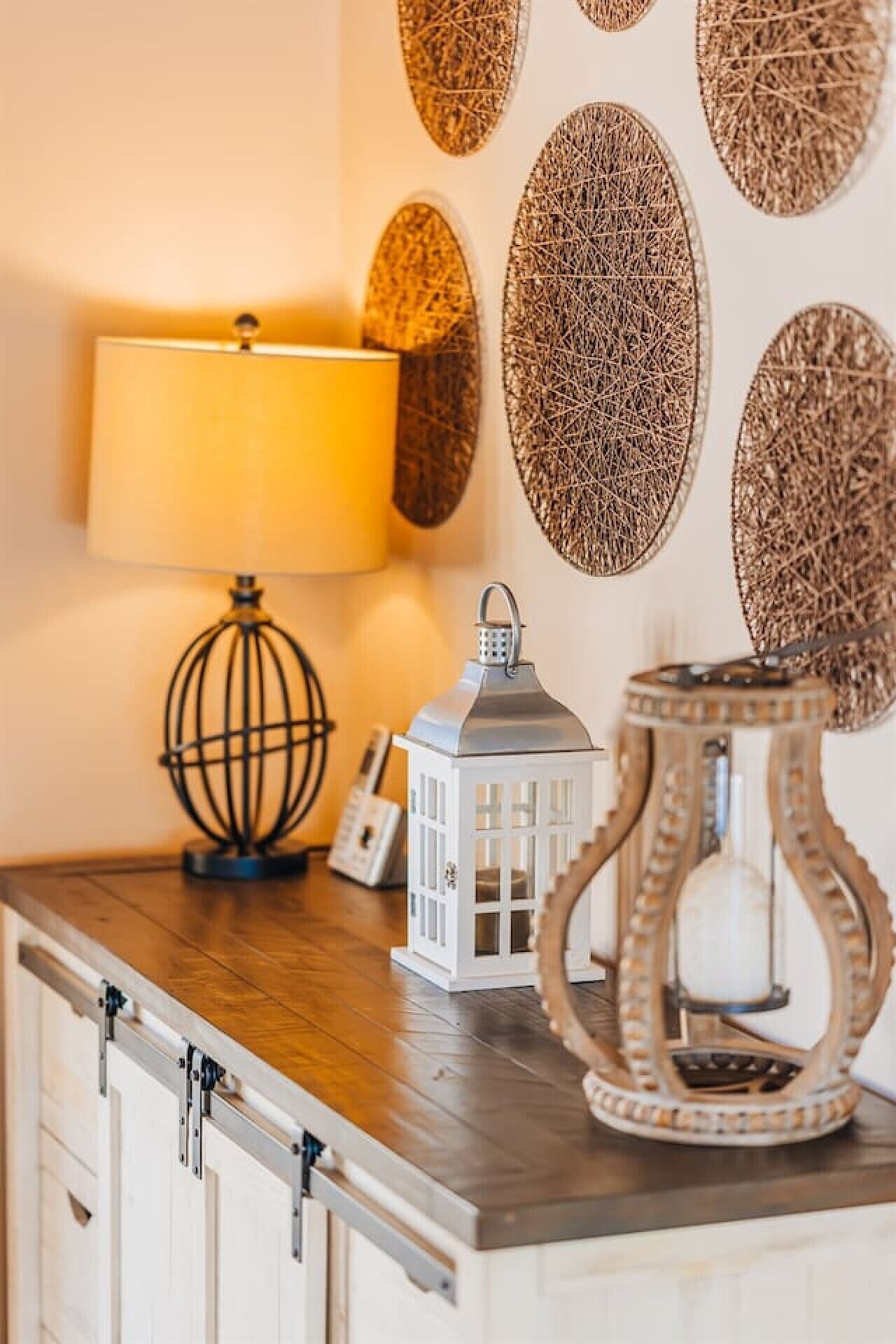 A wooden table with a lamp, a lantern, and wall art.