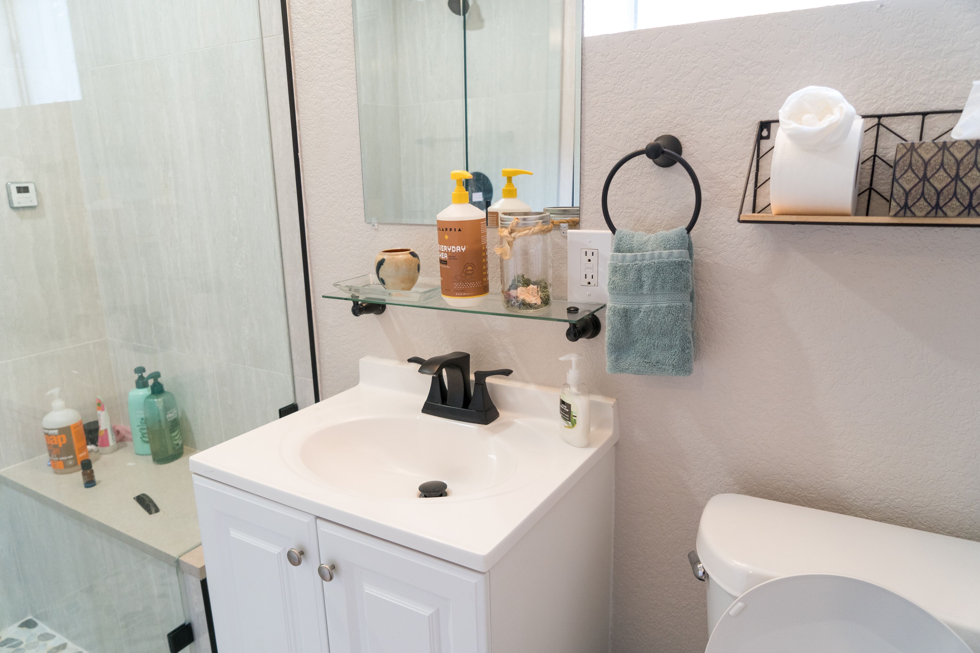 A bathroom with a white sink, a mirror, a towel rack, and toiletries on a shelf.