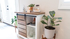Ein weißes Schranksystem mit Holzgriffen und Einlegeböcken, eine Topfpflanze und ein kleiner Tisch mit einer Schüssel und einem Einmachglas.