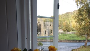 Blick durch ein Fenster auf ein Gebäude aus Stein mit Bögen, eine Wiese und eine Straße.