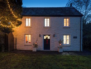 A stone house with a dark entrance, lit windows, and a sign reading "Army Cottage". - Tintern Abbey Cottage (Tintern)