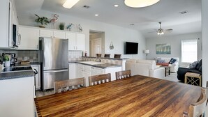 A modern kitchen with white cabinets, stainless steel appliances, and a wooden dining table. - Jamaica Beach Waterfront Home! w/ Paddleboards, Kayak, Pedal Boat, Fishing Gears (Jamaica Beach)