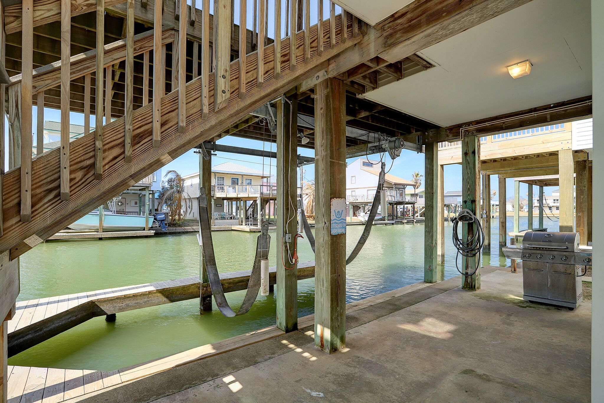 Een houten trap die leidt naar een balkon met uitzicht op een waterpartij, inclusief een barbecue en tuinslangen.