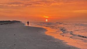 A beach with a sunset, a person running, and waves. - Jamaica Beach Waterfront Home! w/ Paddleboards, Kayak, Pedal Boat, Fishing Gears (Jamaica Beach)