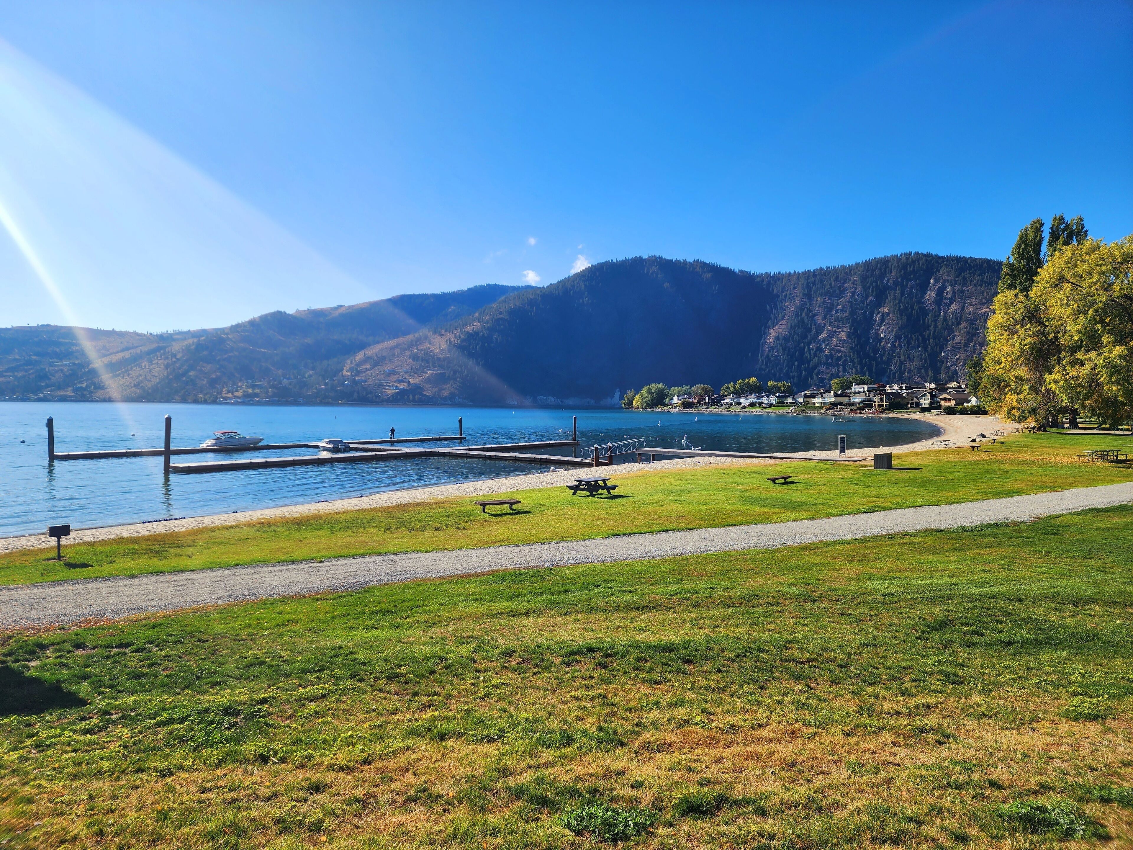 A lakeside park with picnic tables, a boat dock, and a view of a mountain range.