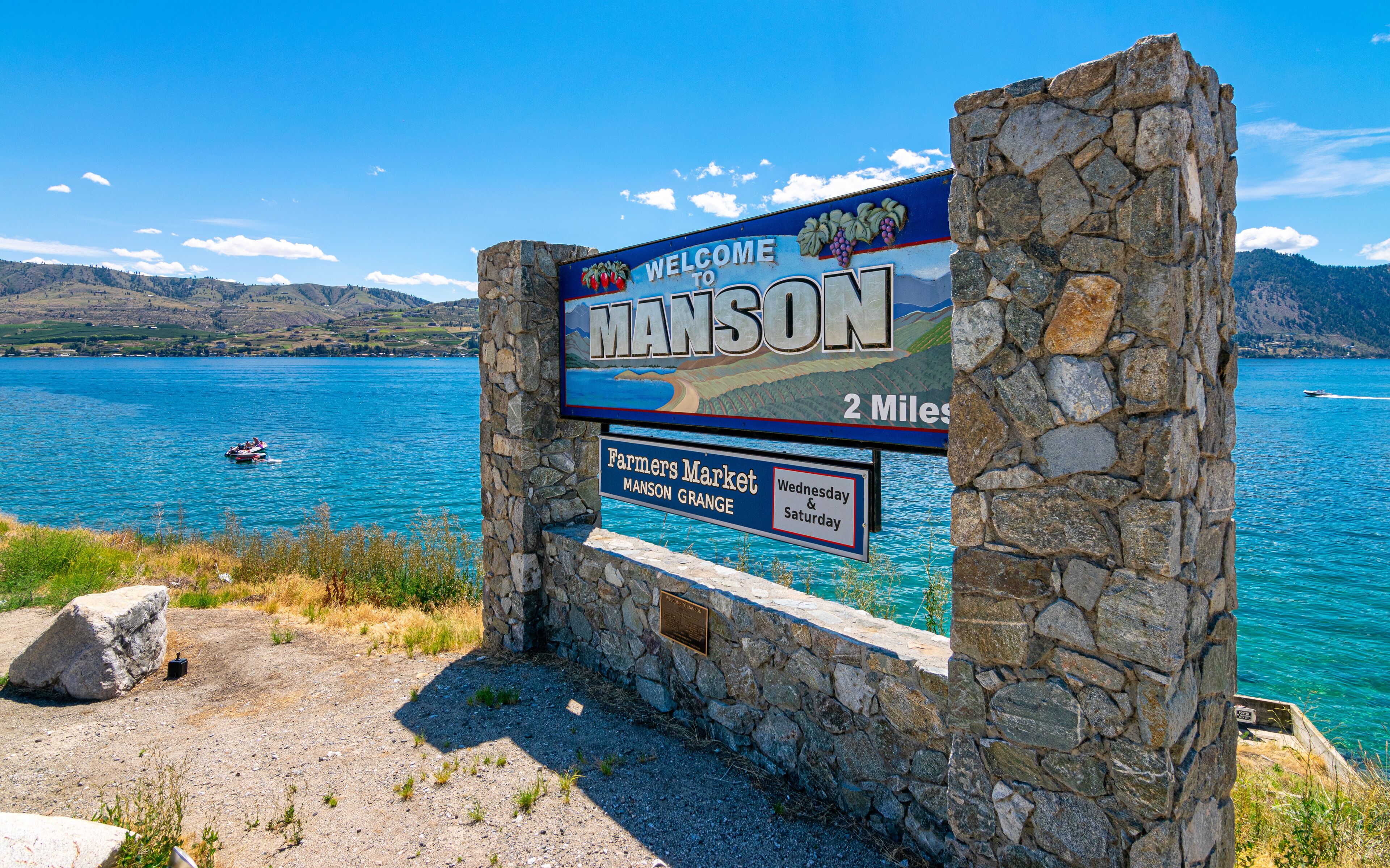 A stone sign with a welcome message to Manson, indicating a Farmers Market and a 2-mile distance.