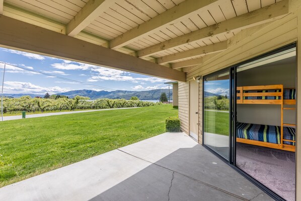 A covered patio with a view of a green lawn and mountains.