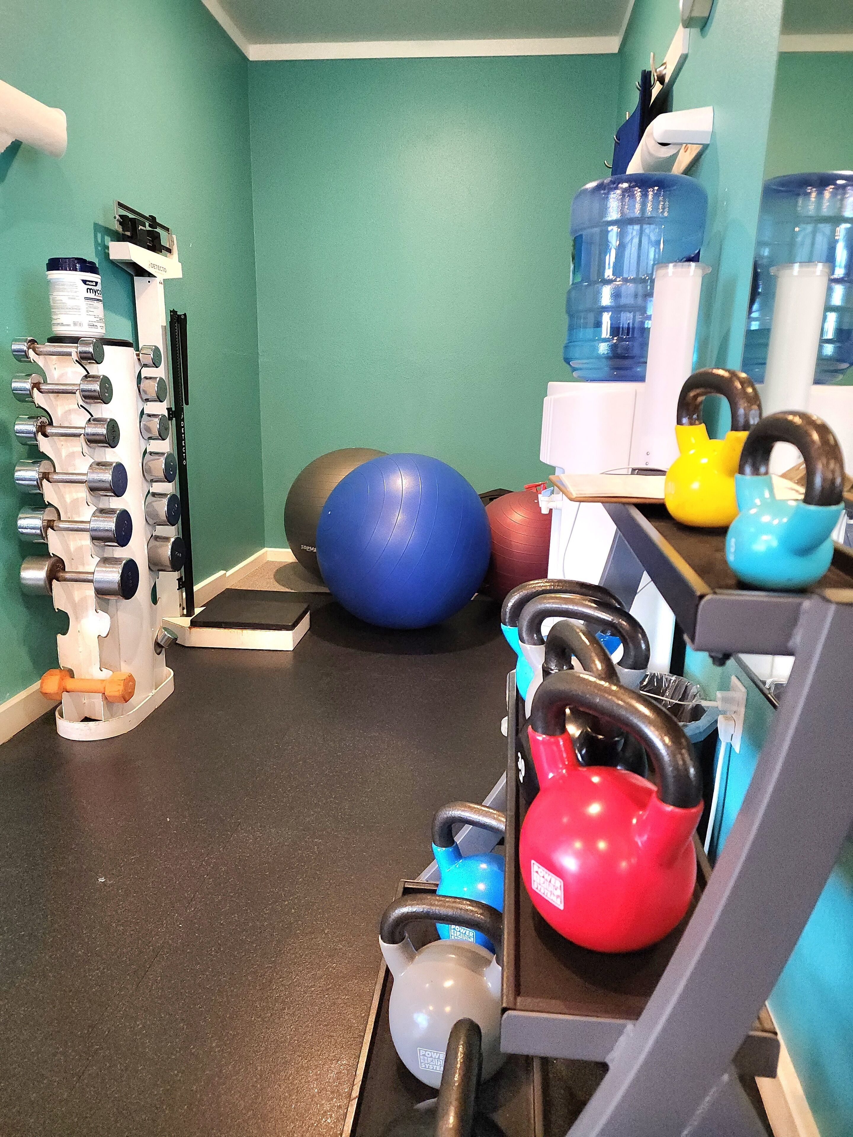 Ett gym med träningsutrustning, inklusive kettlebells, en roddmaskin och träningsbollar.