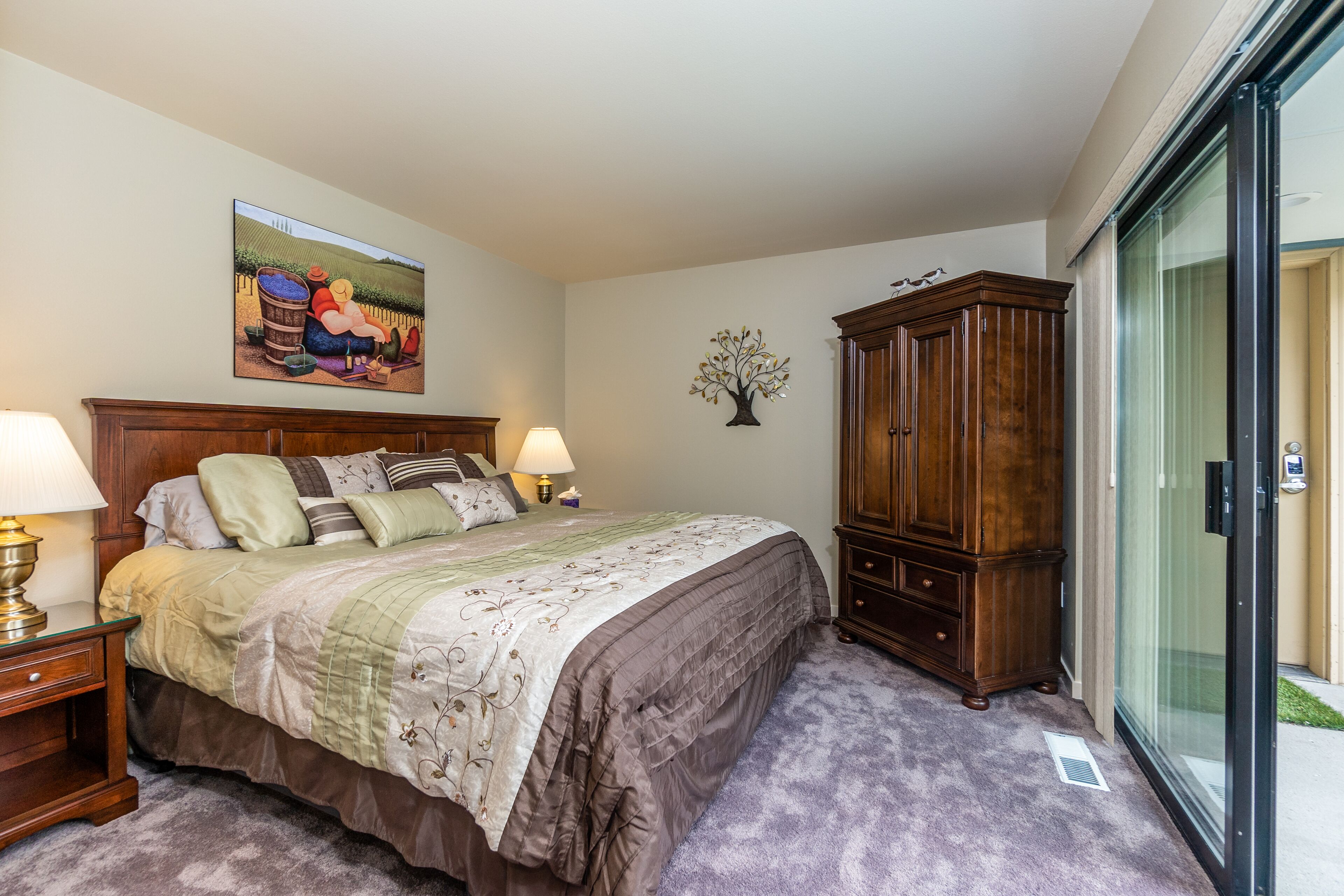 A bedroom with a large bed, two bedside lamps, a wooden cabinet, and a painting on the wall.