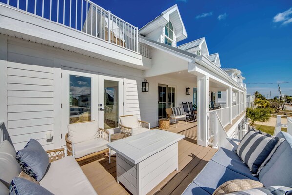 A white two-story house with a covered porch, outdoor furniture, and a view of the ocean.