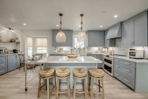 A modern kitchen with a large island, bar stools, pendant lights, and built-in appliances.