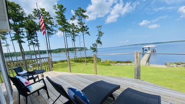 A deck with two wicker chairs and a table, overlooking a lake with a dock and an American flag. - Your Private Coastal NC Waterfront Escape. Dock, deck, sun, peace, REPEAT! (Aurora)
