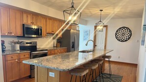 A modern kitchen with wooden cabinets, stainless steel appliances, a granite countertop, and bar stools. - Your Private Coastal NC Waterfront Escape. Dock, deck, sun, peace, REPEAT! (Aurora)