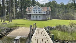 A two-story house with a large deck and a view of a forest. - Your Private Coastal NC Waterfront Escape. Dock, deck, sun, peace, REPEAT! (Aurora)