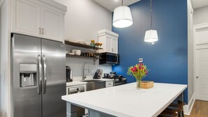 A modern kitchen with stainless steel appliances, a white island with stools, and a blue accent wall. - Home near Superdome and 10 minute drive to French Quarter. (New Orleans)