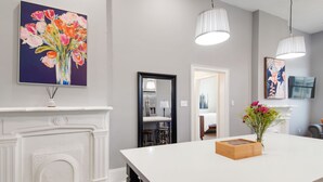 A modern kitchen with a white island, pendant lights, a fireplace, and a painting of flowers. - Home near Superdome and 10 minute drive to French Quarter. (New Orleans)