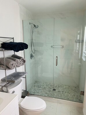 Un baño moderno con ducha de vidrio, inodoro y toallero con toallas dobladas.