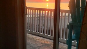 Een kamer met uitzicht op een zonsondergang boven de oceaan, een wit hek en een groene stoel.