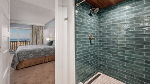 Een slaapkamer met uitzicht op zee, een douche met groene tegels en een houten plafond.
