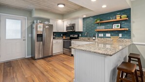 Een moderne keuken met witte kasten, roestvrijstalen apparatuur, een blauwgroene spatwand en een granieten aanrechtblad eiland.