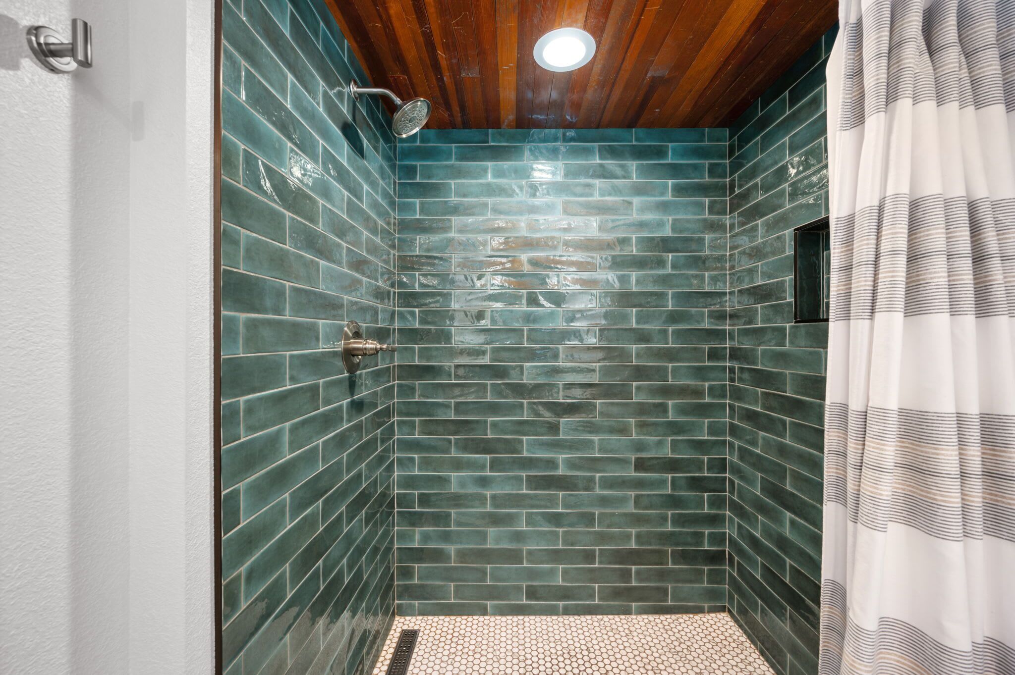 Une douche avec des carreaux verts et un plafond en bois.