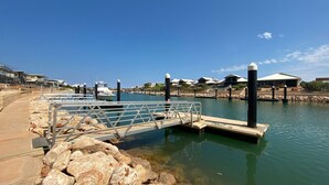 A marina with boats docked, a pedestrian bridge, and modern buildings in the background. - 2 Corella Court - Private Jetty for a boat up to 12mt. (EXMOUTH)