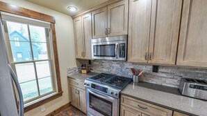A kitchen with wooden cabinets, a stainless steel stove, a microwave, and a toaster. - Historic Elk Ave 3 Master Suites + Hot Tub - Walk Everywhere (Crested Butte)