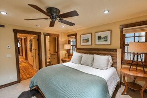 A bedroom with a large bed, a ceiling fan, a wooden headboard, and a window with a view.