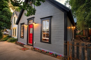 A two-story house with a red door, black-framed windows, and a stone pathway leading to the front door. - Historic Elk Ave 3 Master Suites + Hot Tub - Walk Everywhere (Crested Butte)