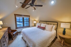 Un dormitorio con una cama grande, un ventilador de techo, una ventana, un aparador y una mesita de noche con una lámpara.