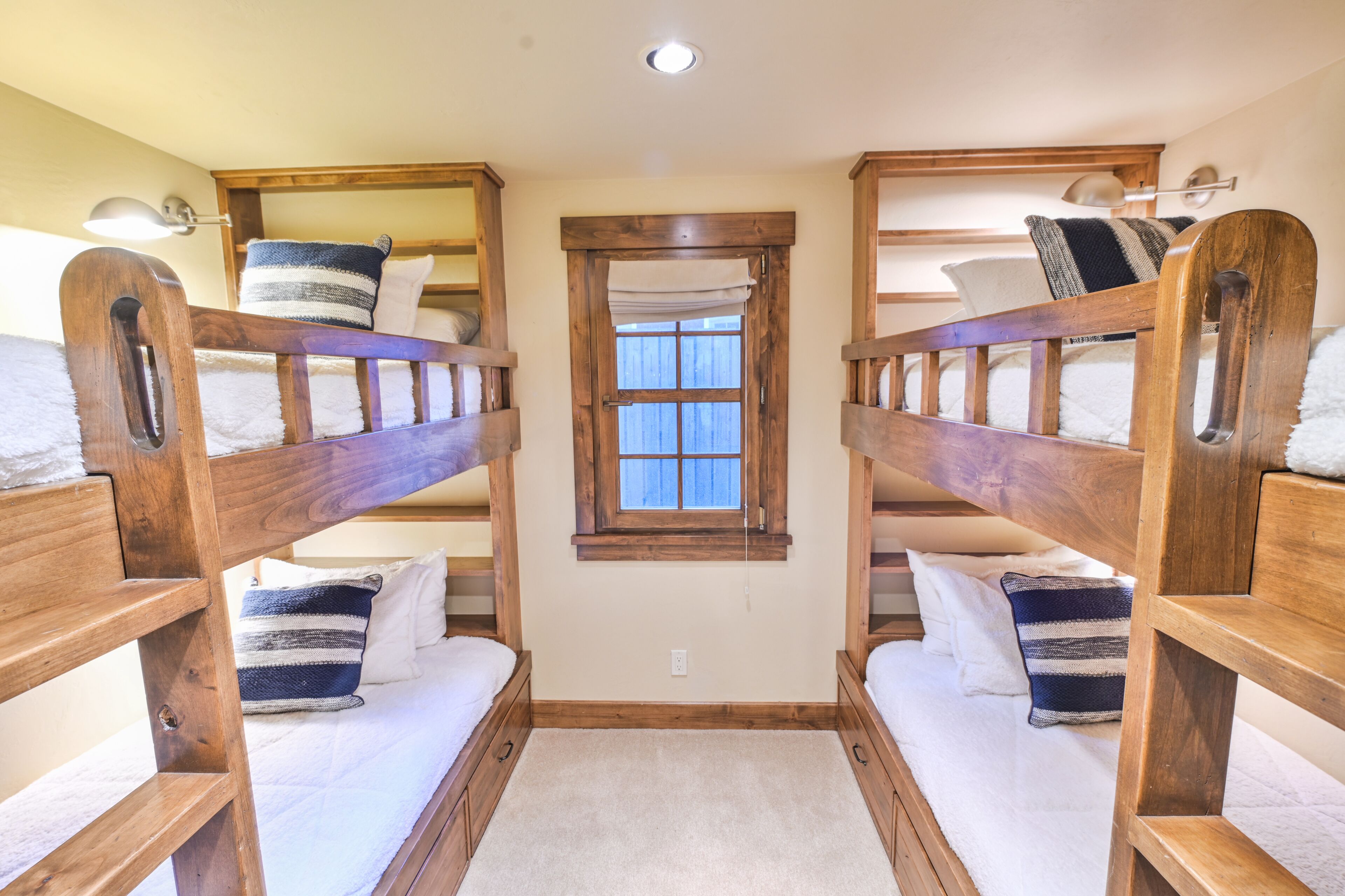 Una habitació amb dos llits superposats, cadascun amb un coixí i una manta. Hi ha una finestra amb cortina al centre.