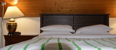 A neatly made bed with green stripes, a wooden headboard, and a lamp on a bedside table.