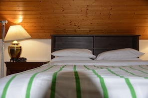 Un lit bien fait, avec des rayures vertes, une tête de lit en bois et une lampe sur une table de chevet.