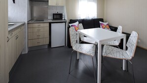 A compact kitchen with a microwave, stove, and refrigerator. There is a dining area with a table and chairs.