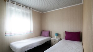 A room with two single beds, a nightstand with a lamp, and a window with sheer curtains.