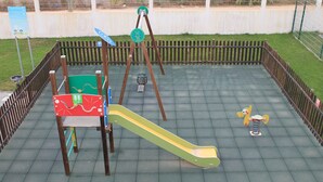 Un parque infantil con tobogán, columpios y balancín.