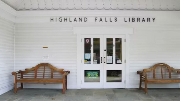 La façade extérieure de la bibliothèque de Highland Falls est blanche. On y voit deux bancs en bois devant l’entrée et une enseigne au-dessus.