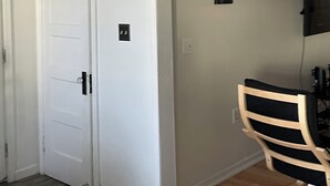 Une pièce avec une porte blanche, un petit tableau accroché au mur et une chaise dotée d’un coussin noir.