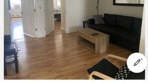 A living room with a black sofa, a wooden coffee table, and a chair. There is a door leading to another room.